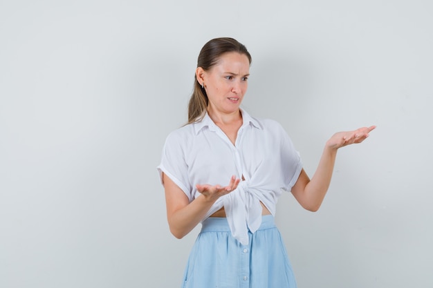 Young female in blouse and skirt stretching hands in questioning manner and looking confused