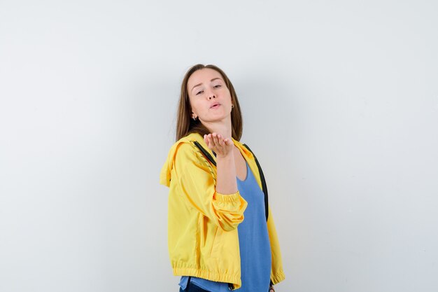 Young female blowing air kiss with pouted lips in t-shirt, jacket and looking cute. front view.