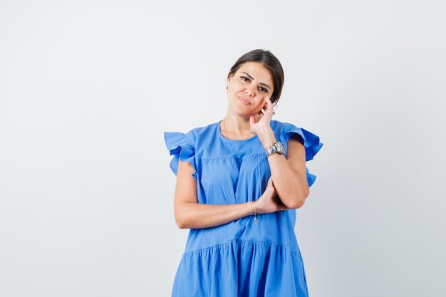 Young female in blue dress standing in thinking pose and looking sensible