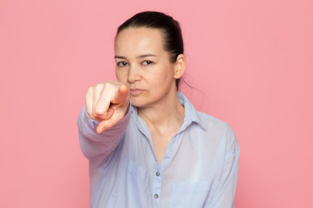 young female in blue shirt posing on the pink wall