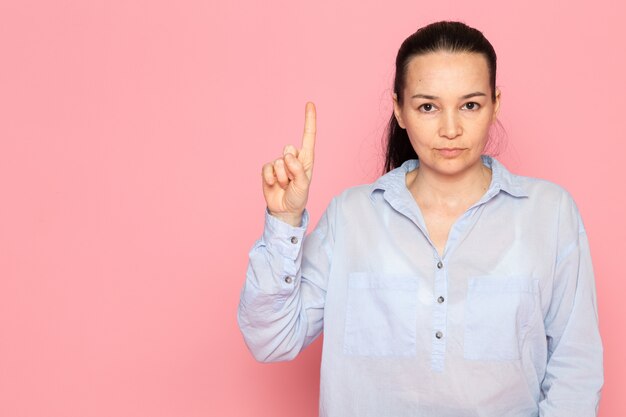 молодая женщина в синей рубашке позирует на розовой стене