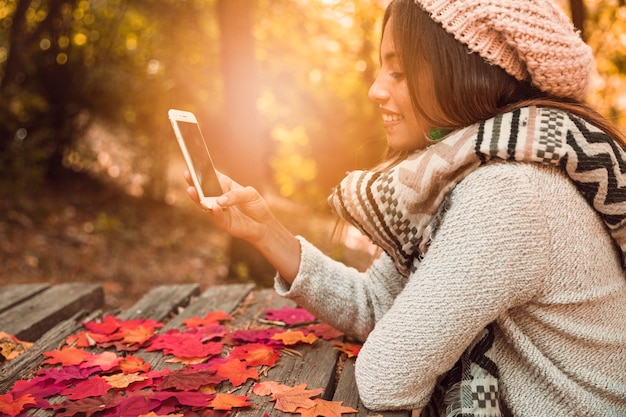 Молодая женщина, просматривая смартфон за столом в Осенний парк