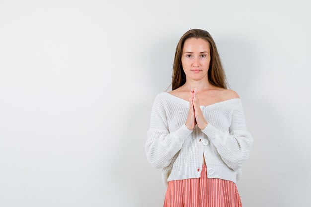 Young female in cardigan and skirt holding hands in praying gesture isolated