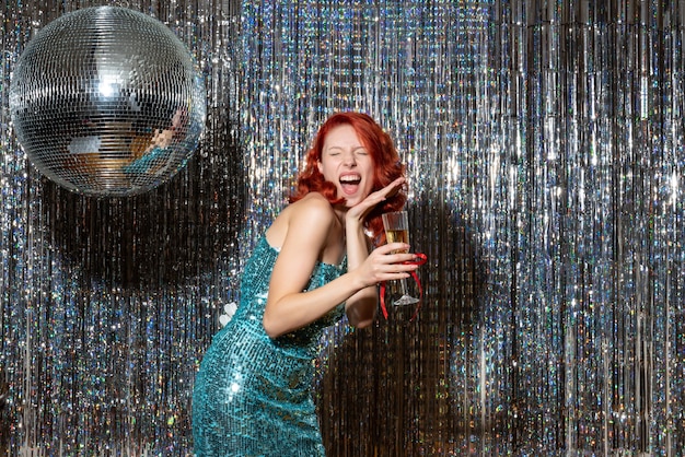 young female celebrating new year in party in beautiful dress on shiny curtains