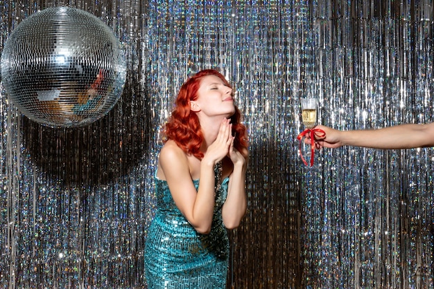 パーティーで新年を祝い、光沢のあるカーテンでシャンパンを取る若い女性