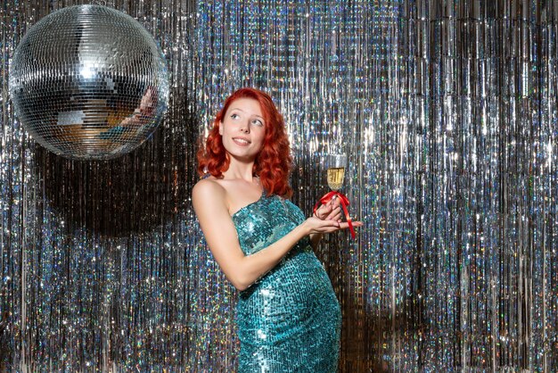 young female celebrating new year in party with disco ball on bright curtains