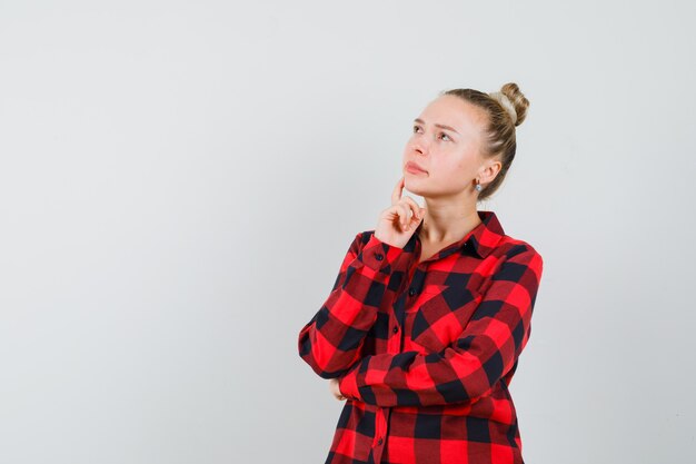 Young female in checked shirt looking up and looking thoughtful , front view.