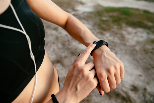 Young female checking the time on her watches after running, outdoors, listening to music