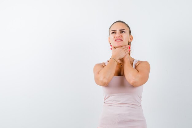 Young female choking herself in white tank top and looking hopeless , front view.