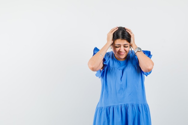 Young female clasping head in hands in blue dress and looking blissful