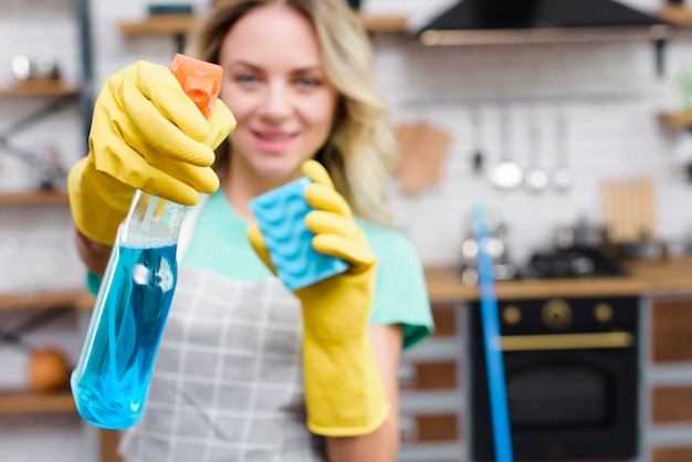 Young female cleaner showing detergent spray bottle