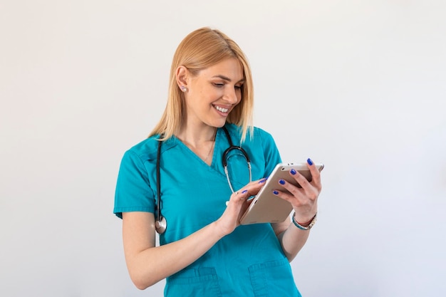 Young female clinician doctor in scrubs using touchpad while communicating with patients online