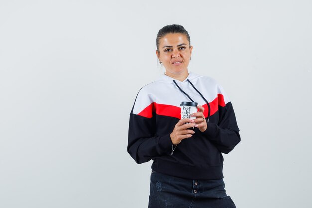 Young female in colorful sweatshirt holding cup while looking at camera , front view. 