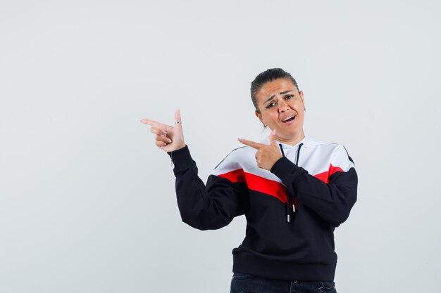 Young female in colorful sweatshirt pointing aside , front view.