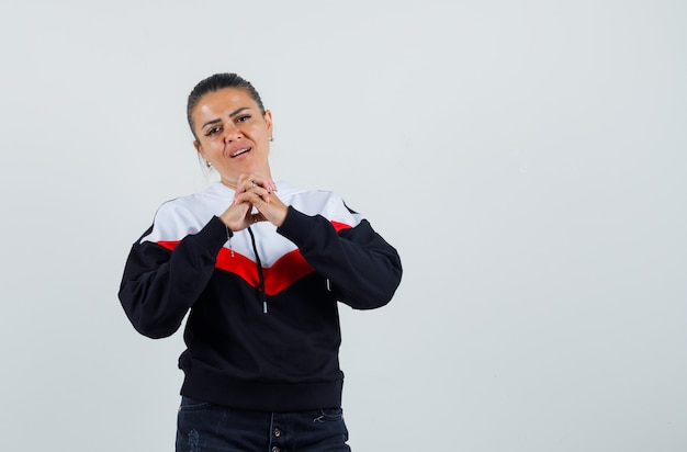 Young female combining her hands in colorful sweatshirt , front view. 