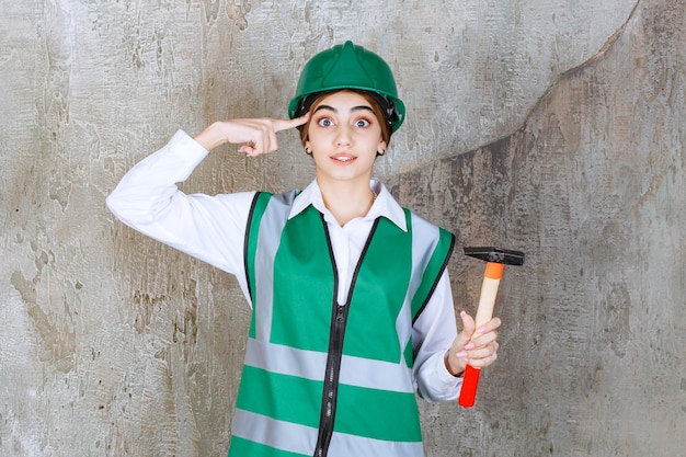 망치로 포즈를 취하는 녹색 헬멧에 젊은 여성 건설 노동자. 고품질 사진