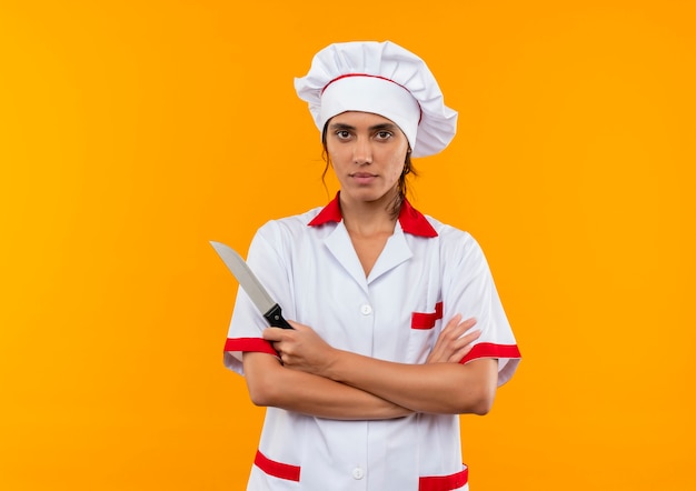 칼을 들고 복사 공간이 격리 된 노란색 벽에 손을 건너 요리사 유니폼을 입고 젊은 여성 요리사