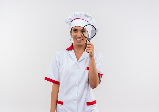 young female cook wearing chef uniform holding magnifier on isolated white wall with copy space