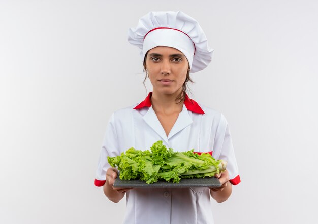 young female cook wearing chef uniform holding salad on cutting board on isolated white wall with copy space