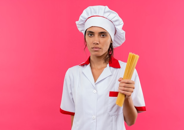 コピースペースと孤立したピンクの壁にスパゲッティを保持しているシェフの制服を着た若い女性料理人