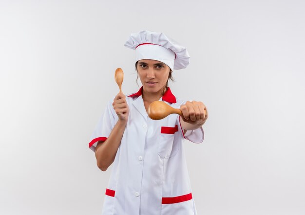 コピースペースと隔離された白い壁にスプーンを保持しているシェフの制服を着た若い女性料理人