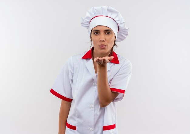 young female cook wearing chef uniform showing kiss gesture on isolated white wall with copy space