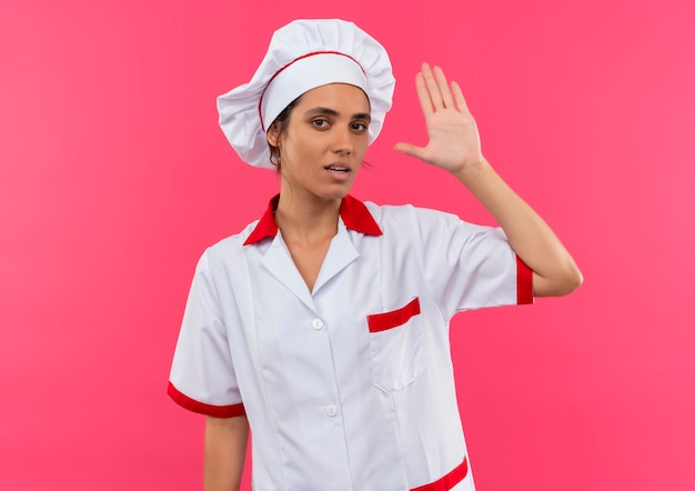  young female cook wearing chef uniform showing stop gesture on isolated pink wall with copy space