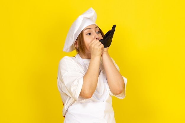 молодая женщина готовит в белом поварском костюме и белой кепке в черной перчатке