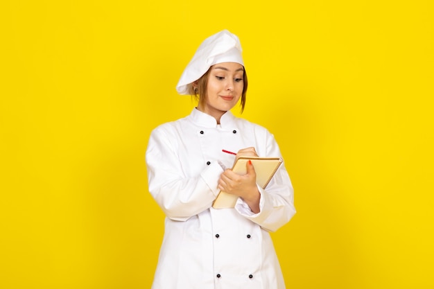 Young female cooking in white cook suit and white cap writing down notes