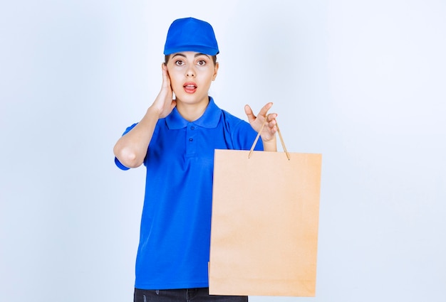 Young female courier carrying paper craft bag and standing on white background.