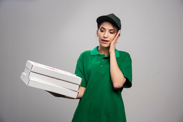 Young female courier posing with pizza boxes and covering her ear. 