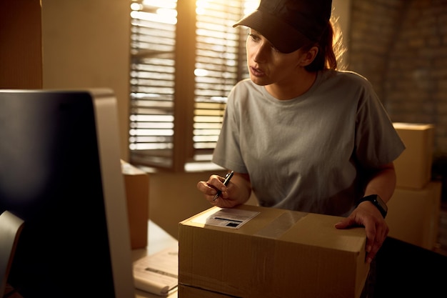 Молодая женщина-курьер с помощью компьютера готовит посылку для доставки в офис