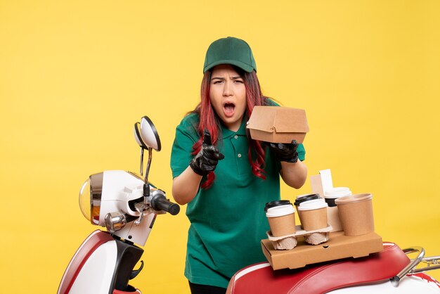 young female courier with delivery coffee and food package on yellow