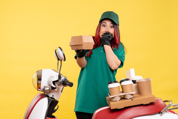 young female courier with delivery coffee and food package on yellow