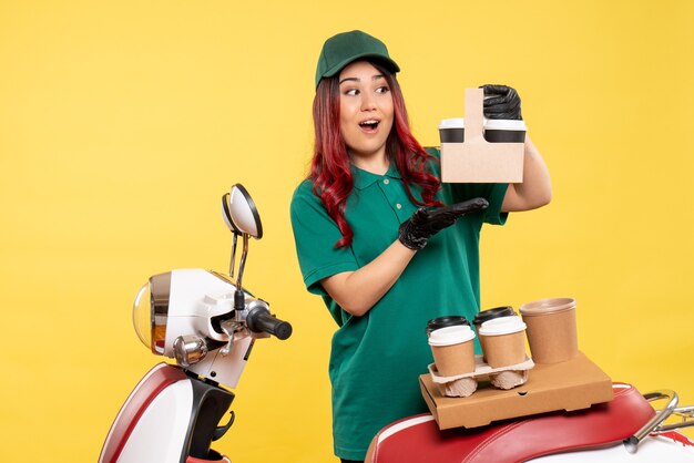 young female courier with delivery coffee on yellow