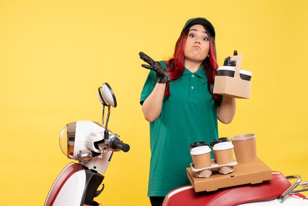 young female courier with delivery coffee on yellow