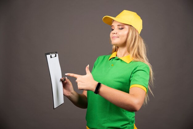 Young female courier with pencil pointing on clipboard. 