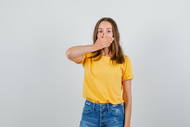 Free photo young female covering mouth with hand in t-shirt, shorts and looking silent. front view.