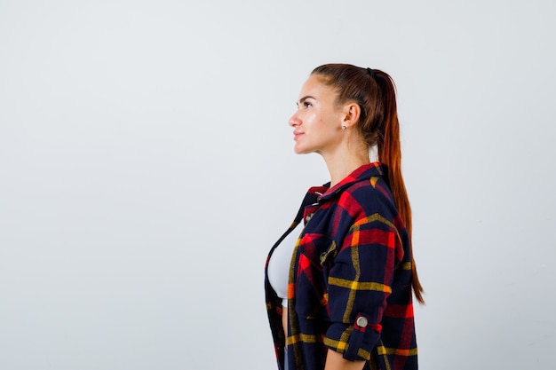 Giovane donna in crop top, camicia a scacchi, pantaloni che guardano lontano e sembrano fiduciosi, vista frontale.