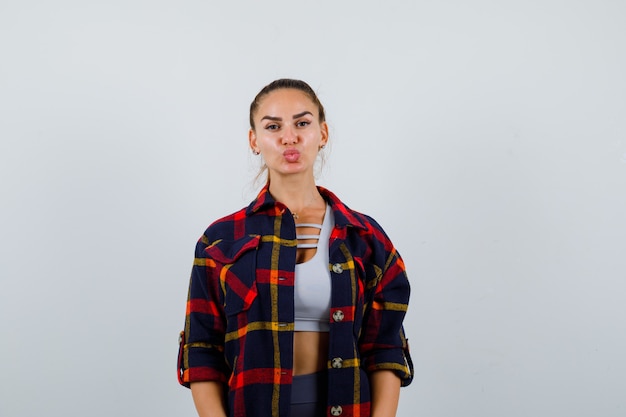 クロップトップの若い女性、唇をふくれっ面とキュートに見える市松模様のシャツ、正面図。