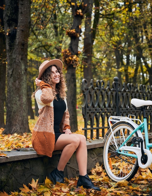 Giovane ciclista femminile che riposa sul marciapiede vicino alla bici in autunno