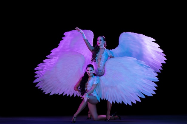 Young female dancer with angel's wings in neon light on black wall