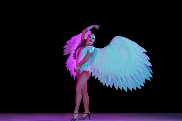 검은 벽에 네온 불빛에 천사의 날개를 가진 젊은 여성 댄서