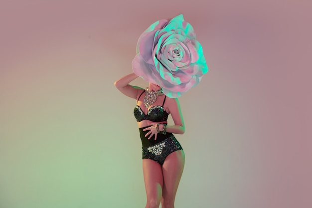 Young female dancers with huge floral hats in neon light on gradient wall