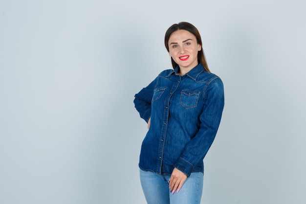 Young female in denim shirt and jeans holding hand on hip while posing and looking charming