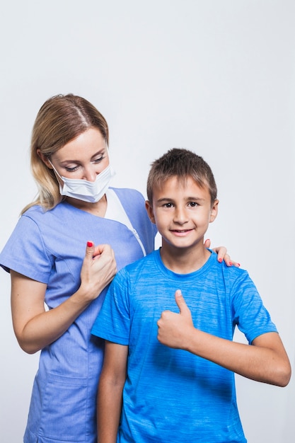 Young female dentist and boy gesturing thumbs up on white backdrop