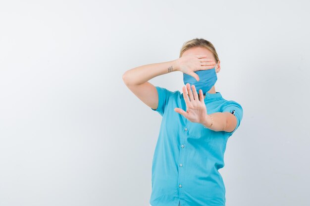 Young female doctor covering eyes with hands while showing stop gesture isolated