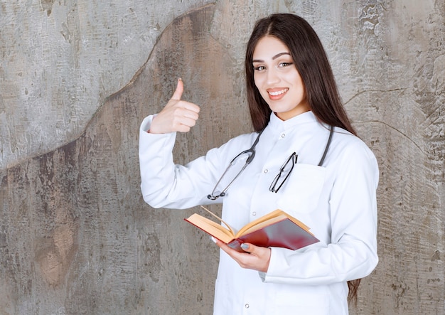 Foto gratuita giovane dottoressa che gesturing pollice in su sul muro grigio