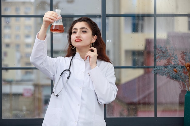 Foto gratuita giovane medico femminile che tiene la bottiglia chimica e lo guarda pensieroso