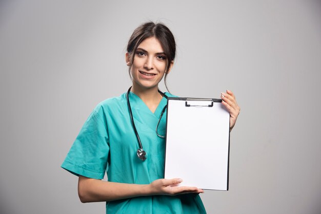 Young female doctor holding clipboard on gray